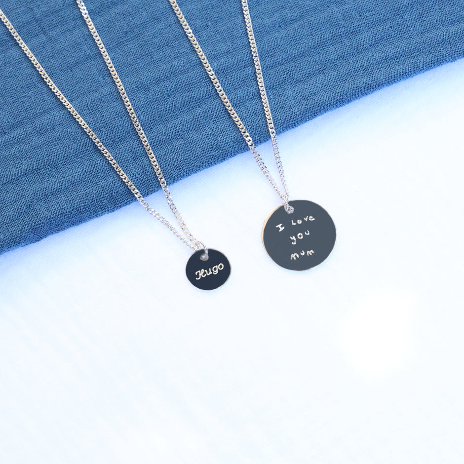 Two silver necklaces with round silver pendants engraved with a name and a handwritten message.