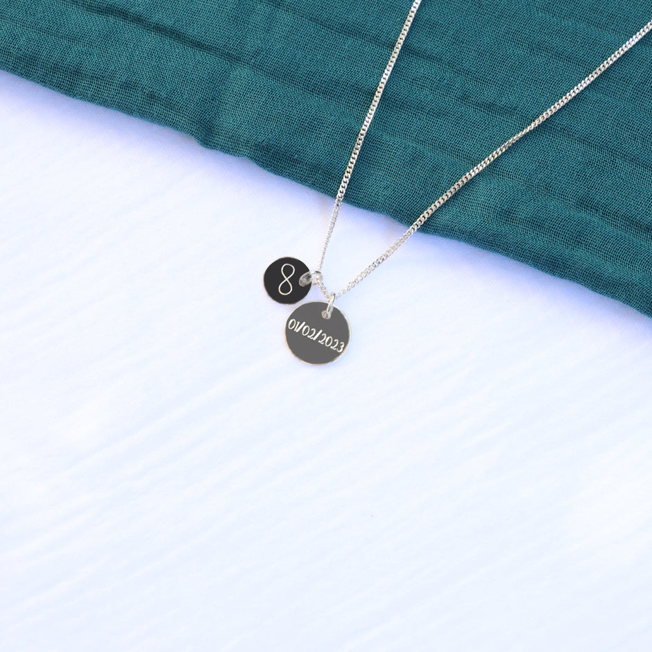 Necklace with two silver pendants, one engraved with a symbol the other with a date 