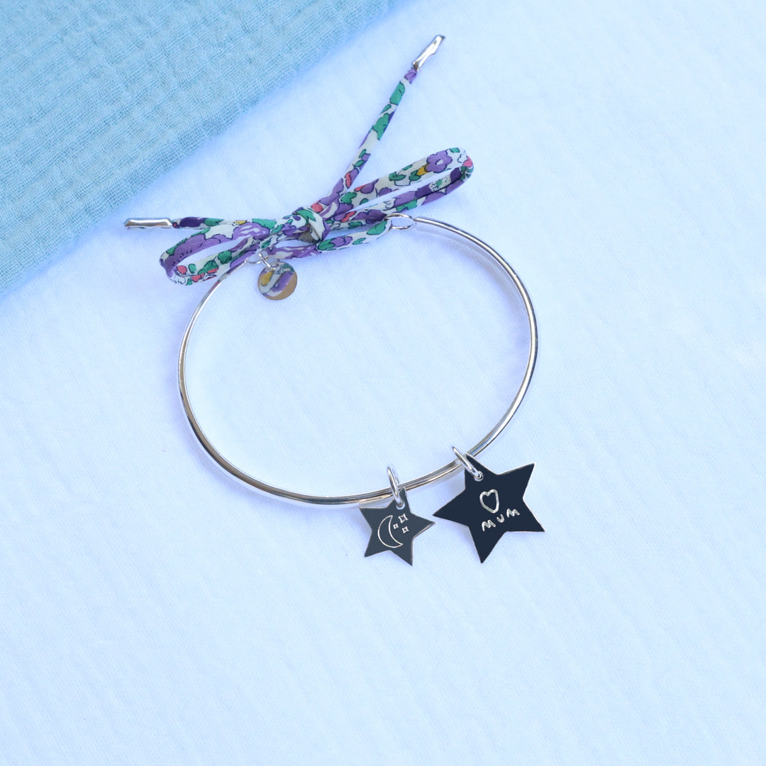 Silver bangle with star-shaped charms engraved with moon symbol and child's handwritten message