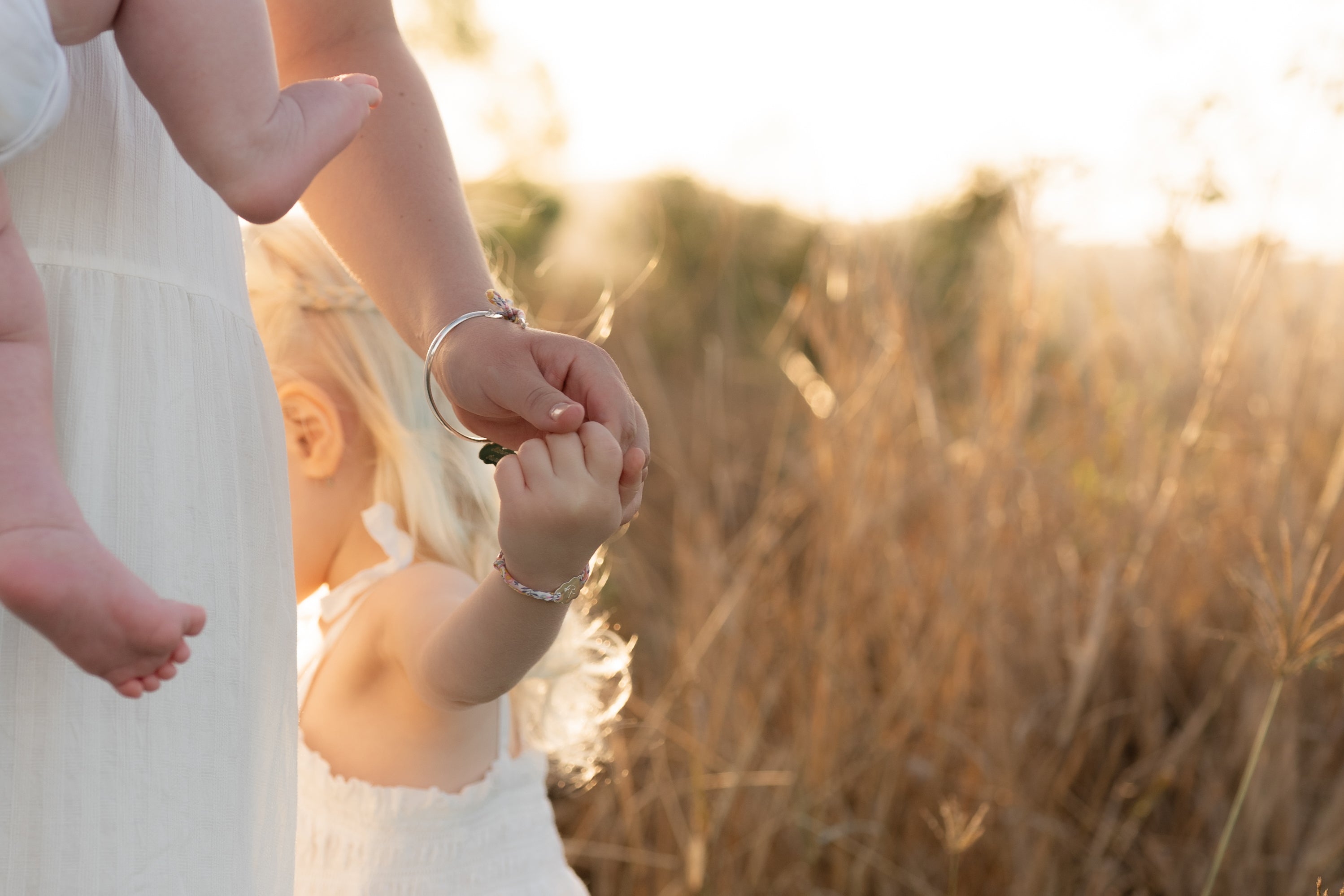 Child holding mummy's hand with baby in her arms. The mum is wearing a bangle with a fabric bow and a custom engraved pendant.