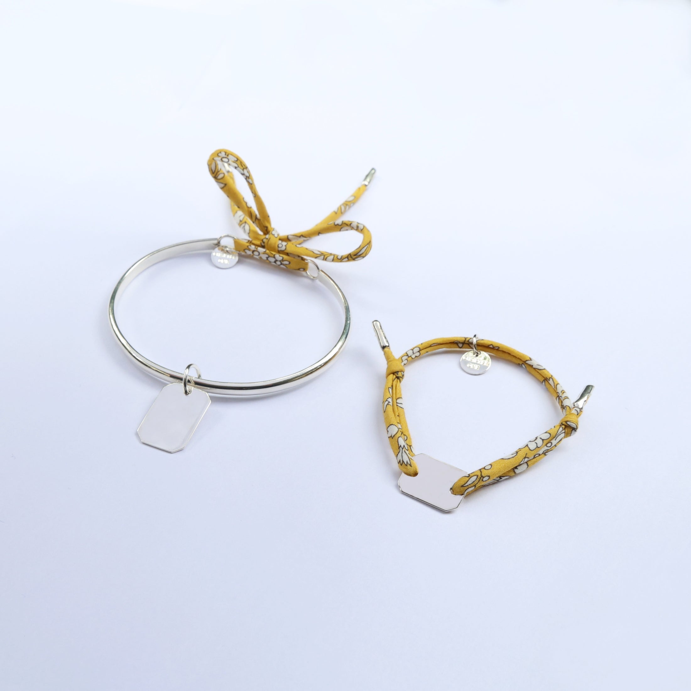 Two bracelets, one silver bangle and one cord bracelet with floral pattern, with bar pendants, perfect for mums and their little ones