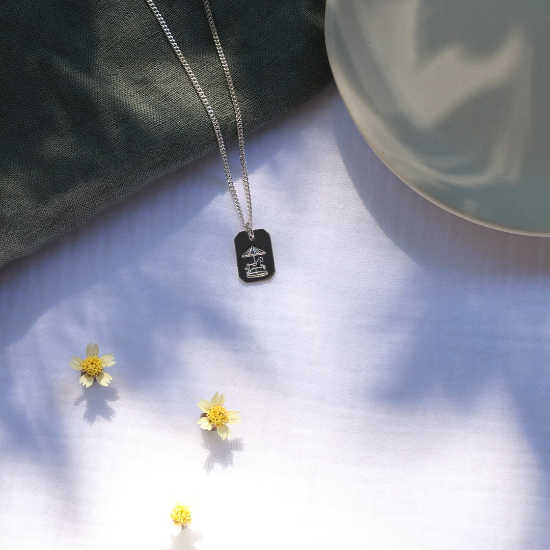 Silver necklace with an engraved pendant on a white surface with yellow flowers.