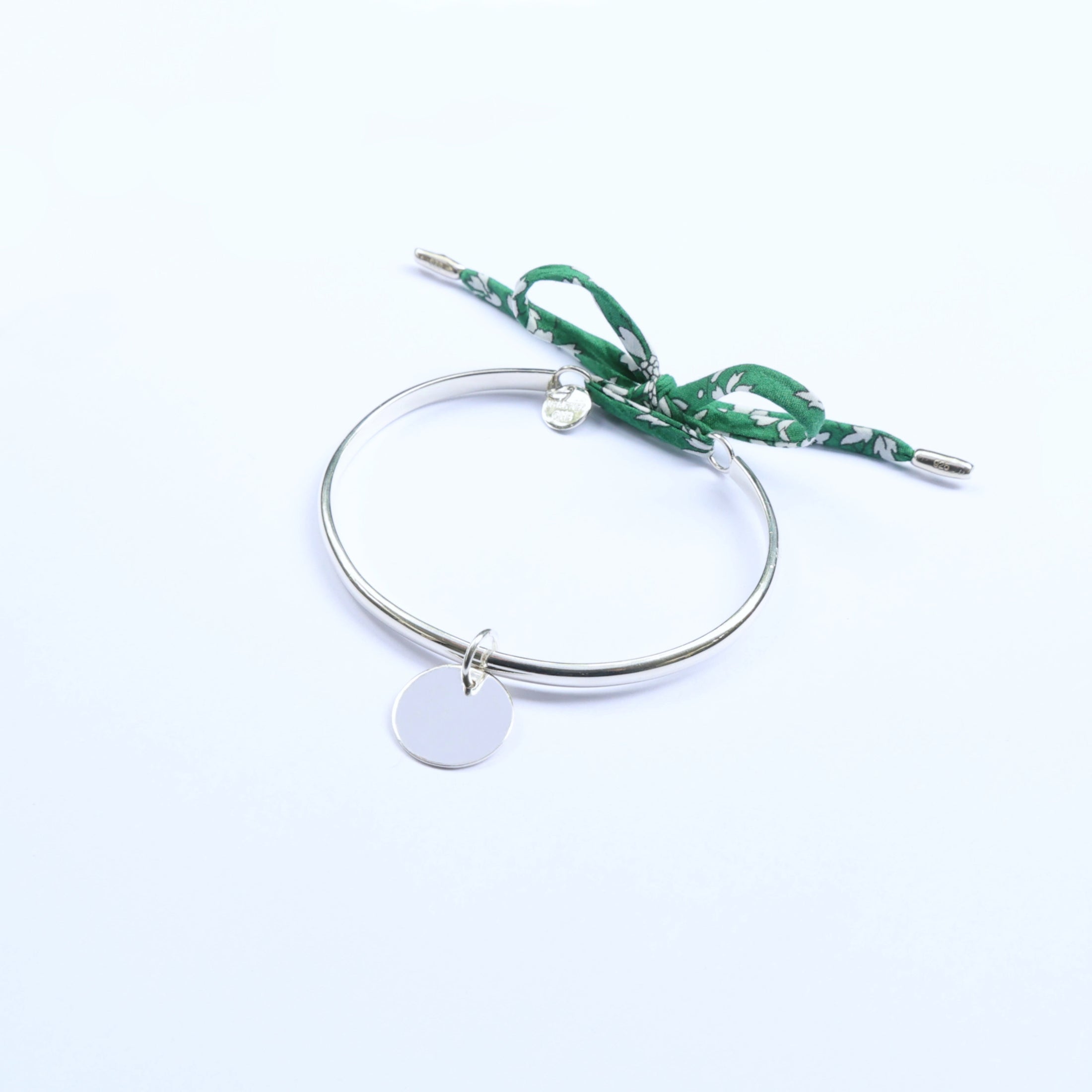 Silver bangle with a green cord and a round charm